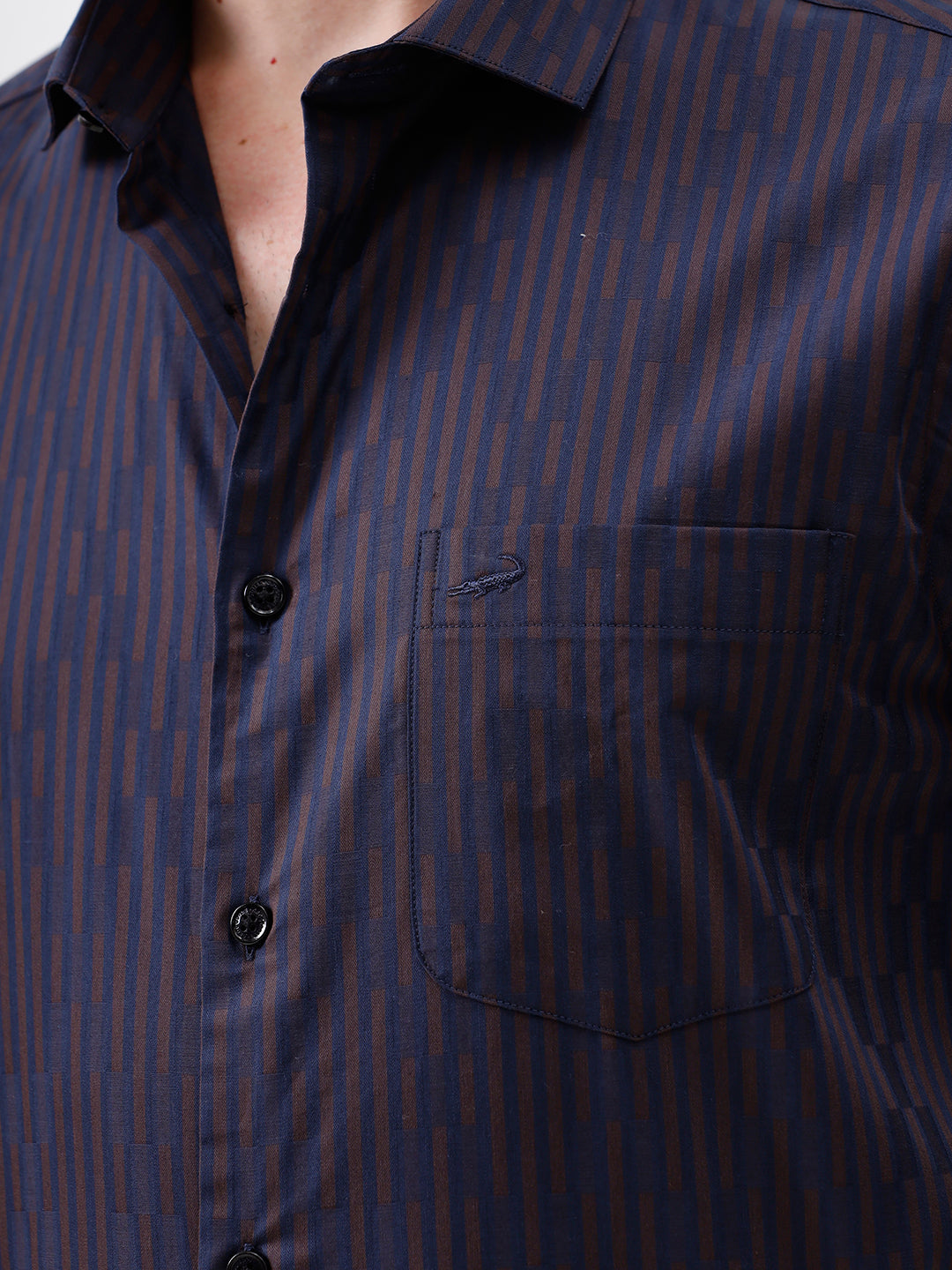 A man wearing a dark navy blue button-down shirt with thin vertical red stripes and light brown trousers, standing against a plain white studio background.