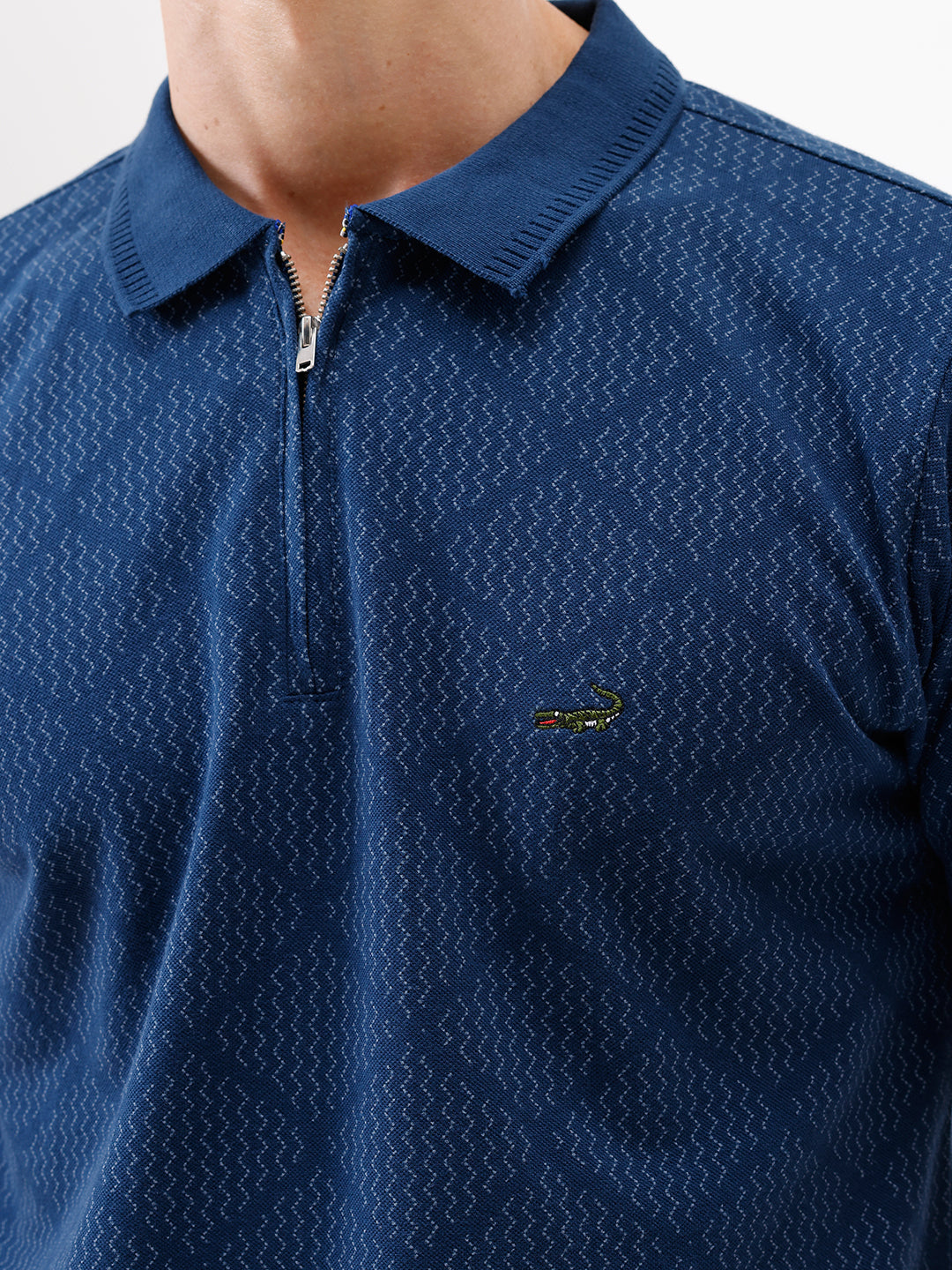 A man wearing a navy blue short-sleeve polo shirt with a subtle geometric pattern and a half-zip collar, paired with gray trousers, against a plain white background.