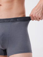 Gray boxer briefs with a brand logo on the waistband, held by a hand against a neutral background.