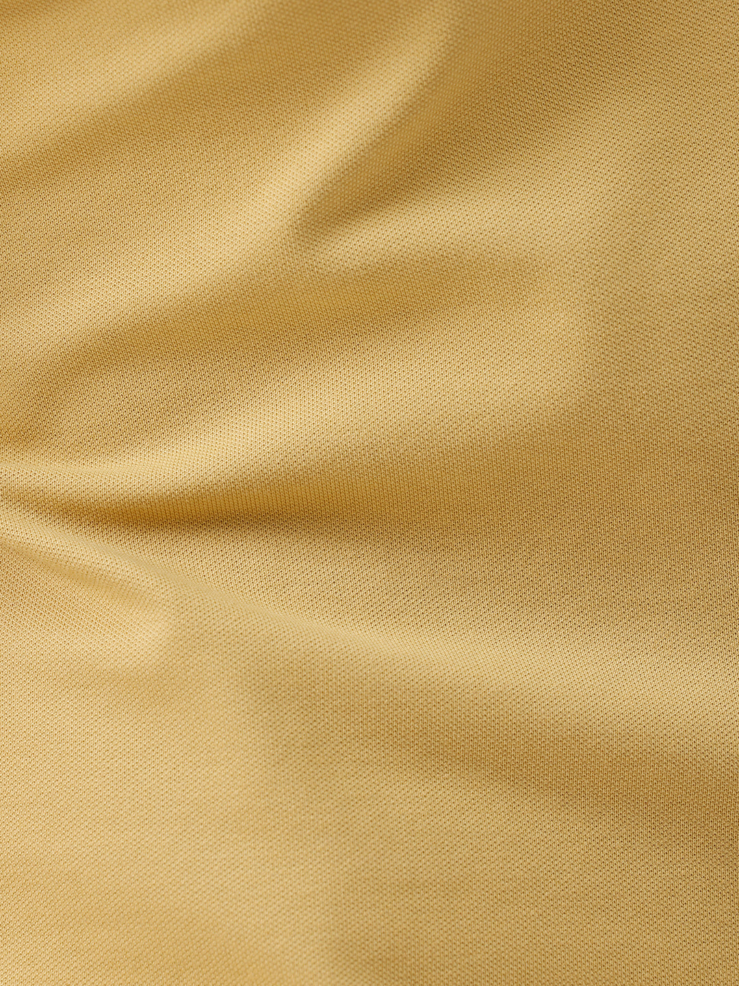 A man wearing a light yellow Lacoste polo shirt with dark piping on the collar and sleeve cuffs, paired with beige trousers, against a plain white studio background.
