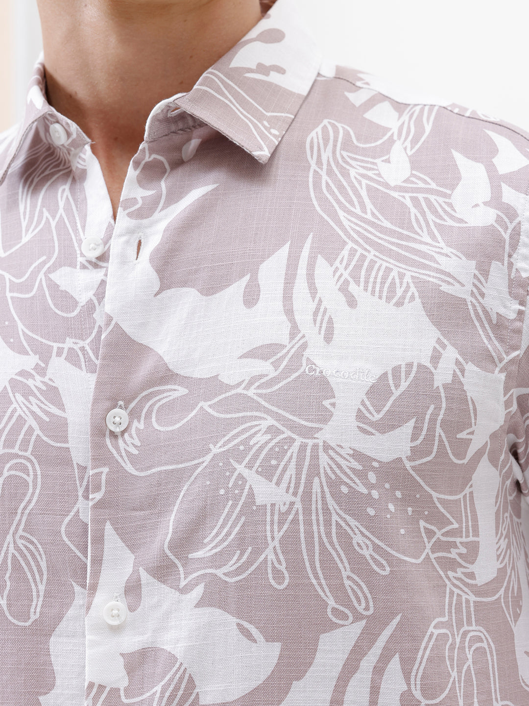 A man wearing a long-sleeve button-up shirt with a light gray and white abstract floral pattern, paired with dark blue jeans, standing against a plain white background.