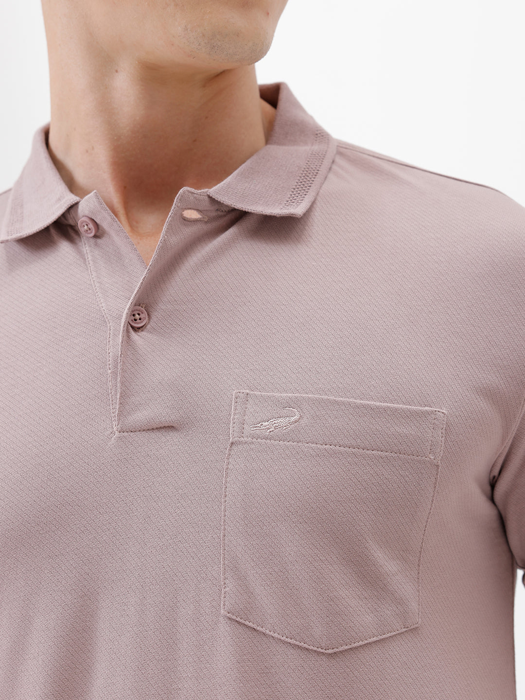 A man modeling a short-sleeve polo shirt in a dusty mauve-pink color, paired with khaki cargo pants and a baseball cap, against a plain light gray background.