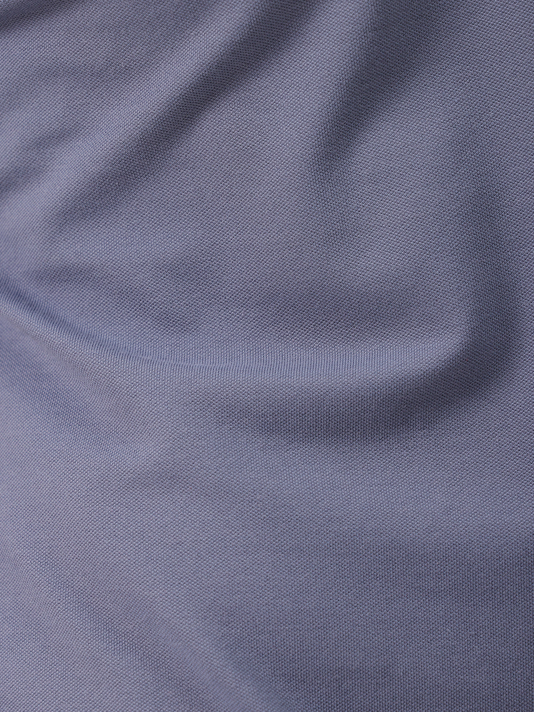 A man wearing a slate blue polo shirt and beige trousers, standing against a plain white background.
