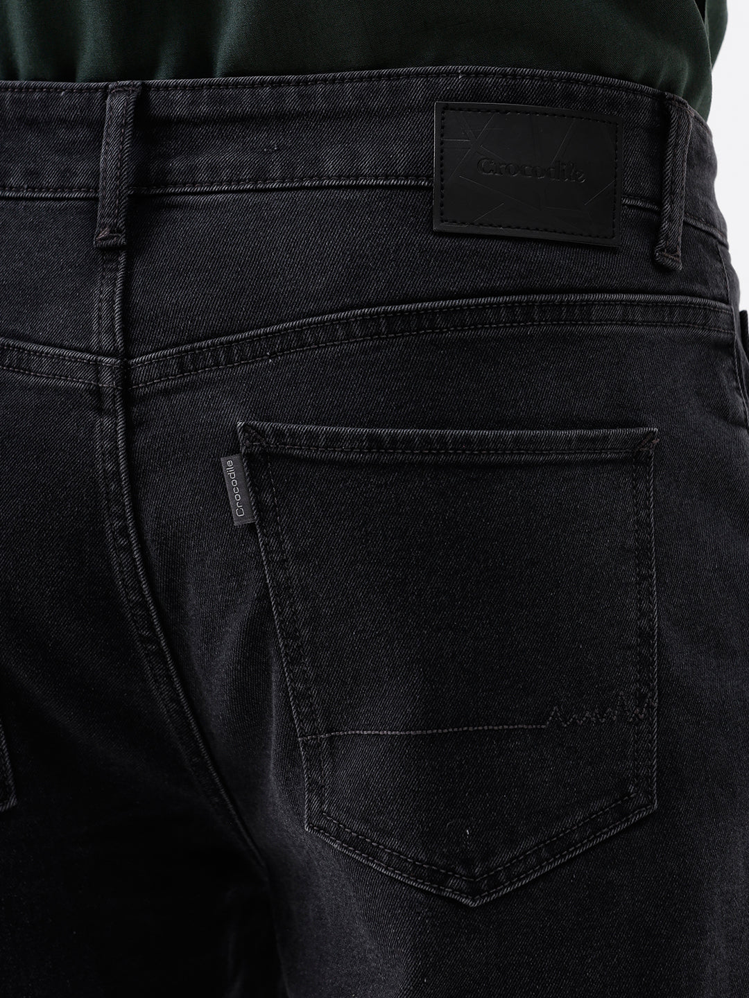 A person wearing dark washed denim jeans, a dark green shirt, and white sneakers, shown from the chest down against a plain light gray studio background.