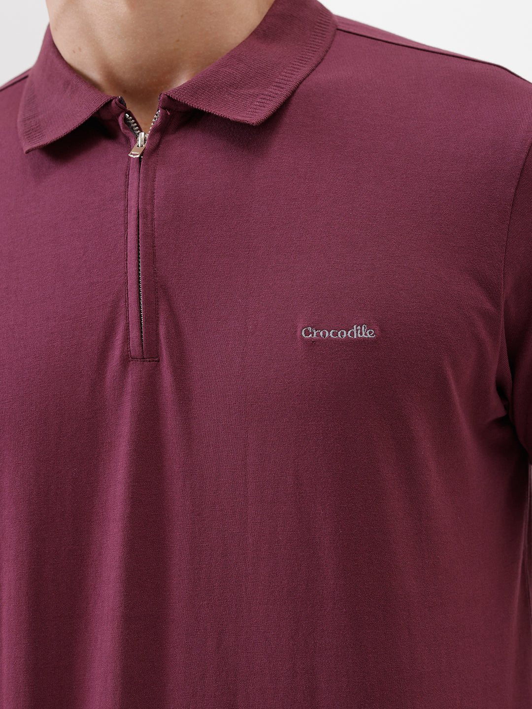A man wearing a short-sleeve polo shirt in maroon with gray sleeve trim and a half-zip collar, paired with beige cargo pants, against a plain white studio background.