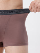 Brown boxer briefs with black waistband held by a hand on a white background