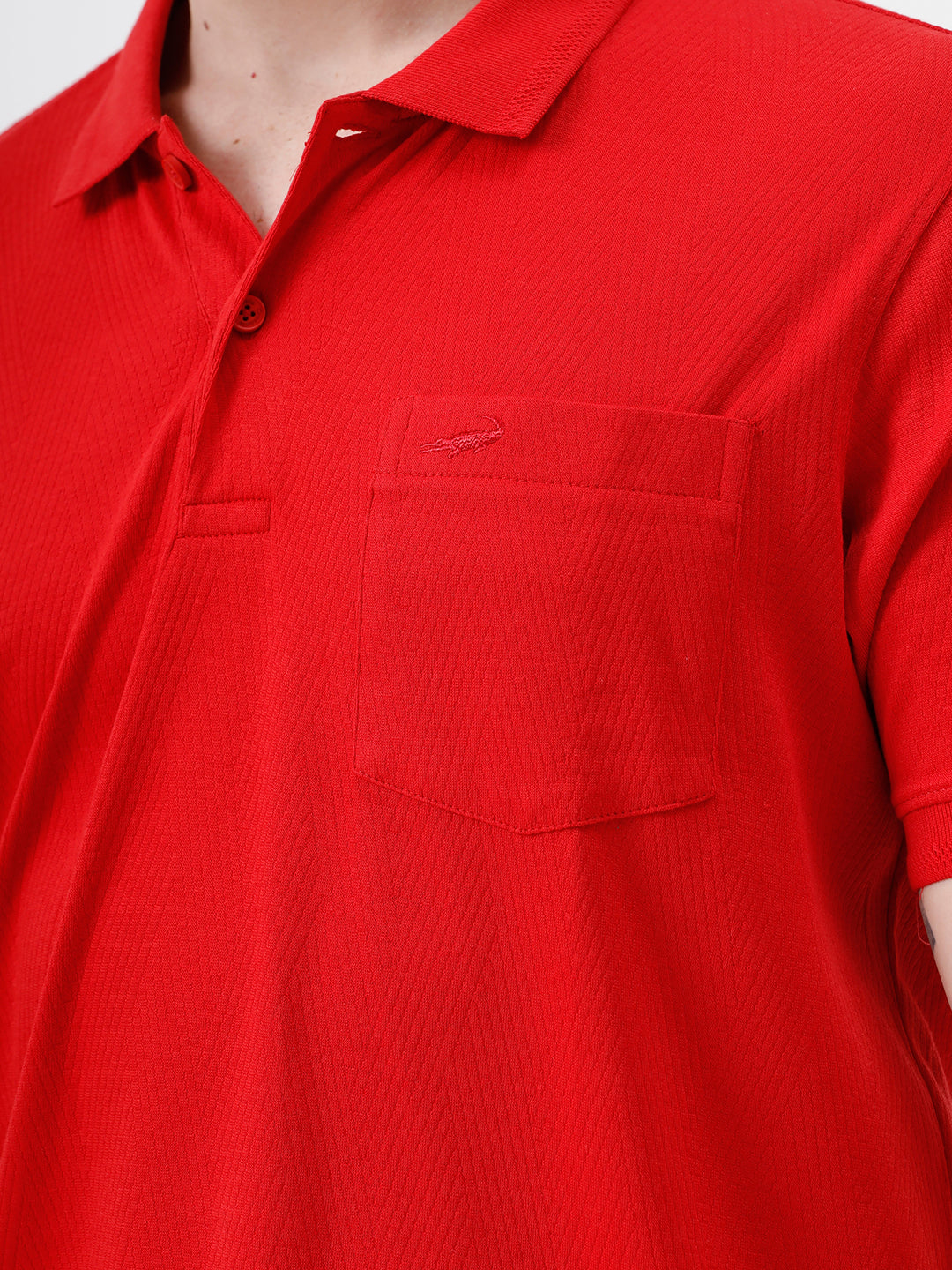 A man wearing a bright red short-sleeve polo shirt with a chest pocket, paired with beige trousers, standing against a plain white studio background.