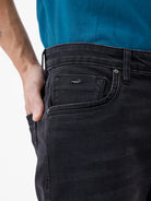 A person wearing slim-fit black jeans, a teal t-shirt, and white sneakers with gray accents, standing against a clean white studio background.