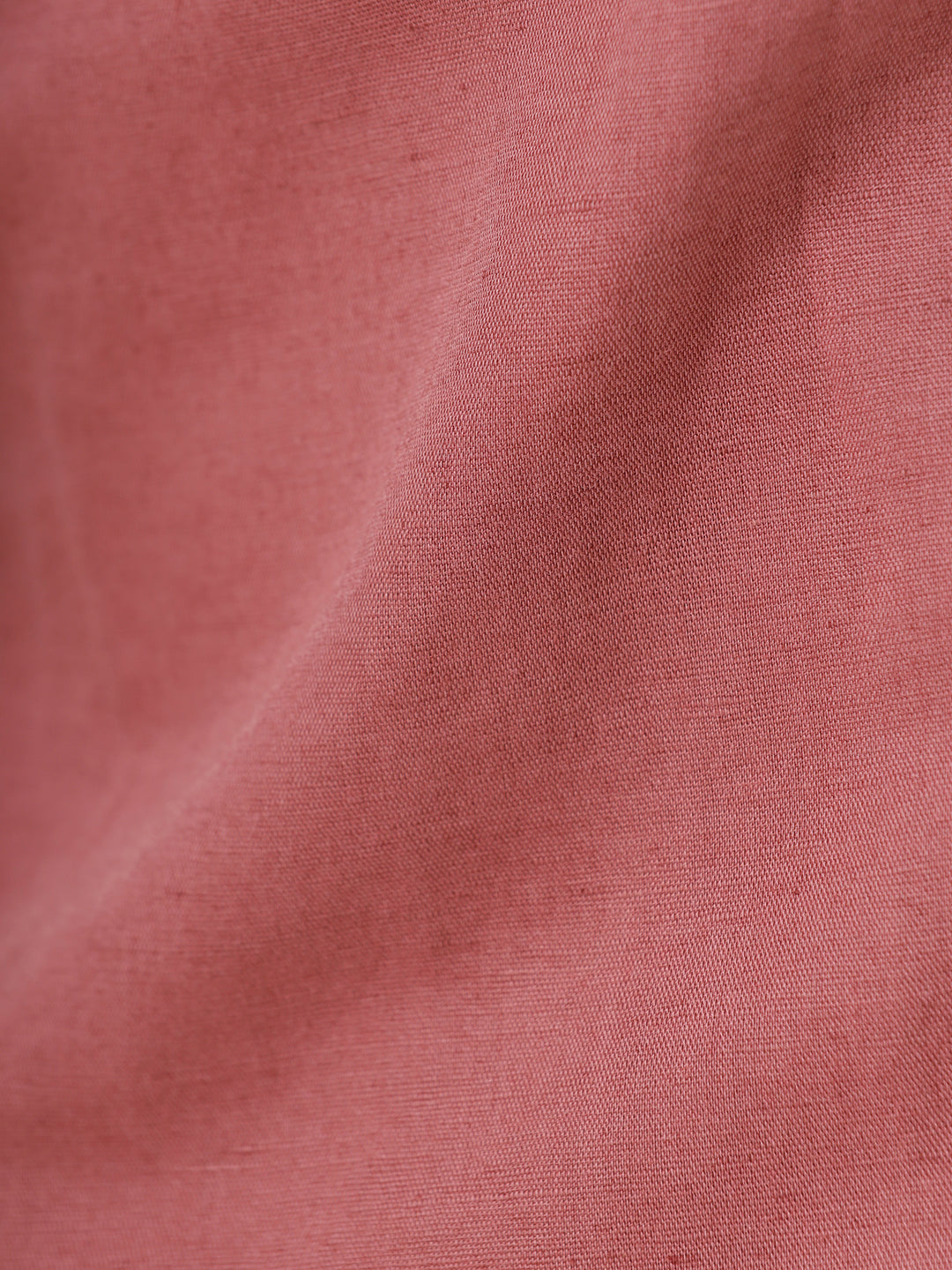 A man wearing a short-sleeve button-up shirt in a dusty rose color, paired with beige trousers, standing against a light gray studio background.