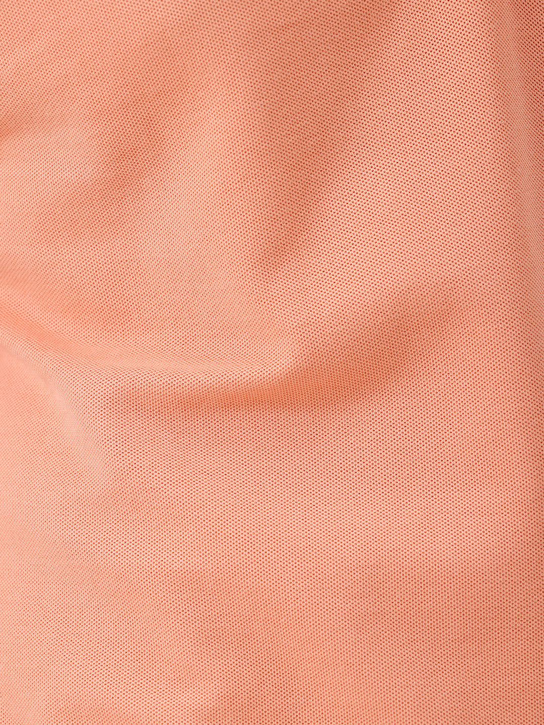 A man wearing a peach-colored short-sleeve polo shirt and beige trousers, standing against a plain white studio background.