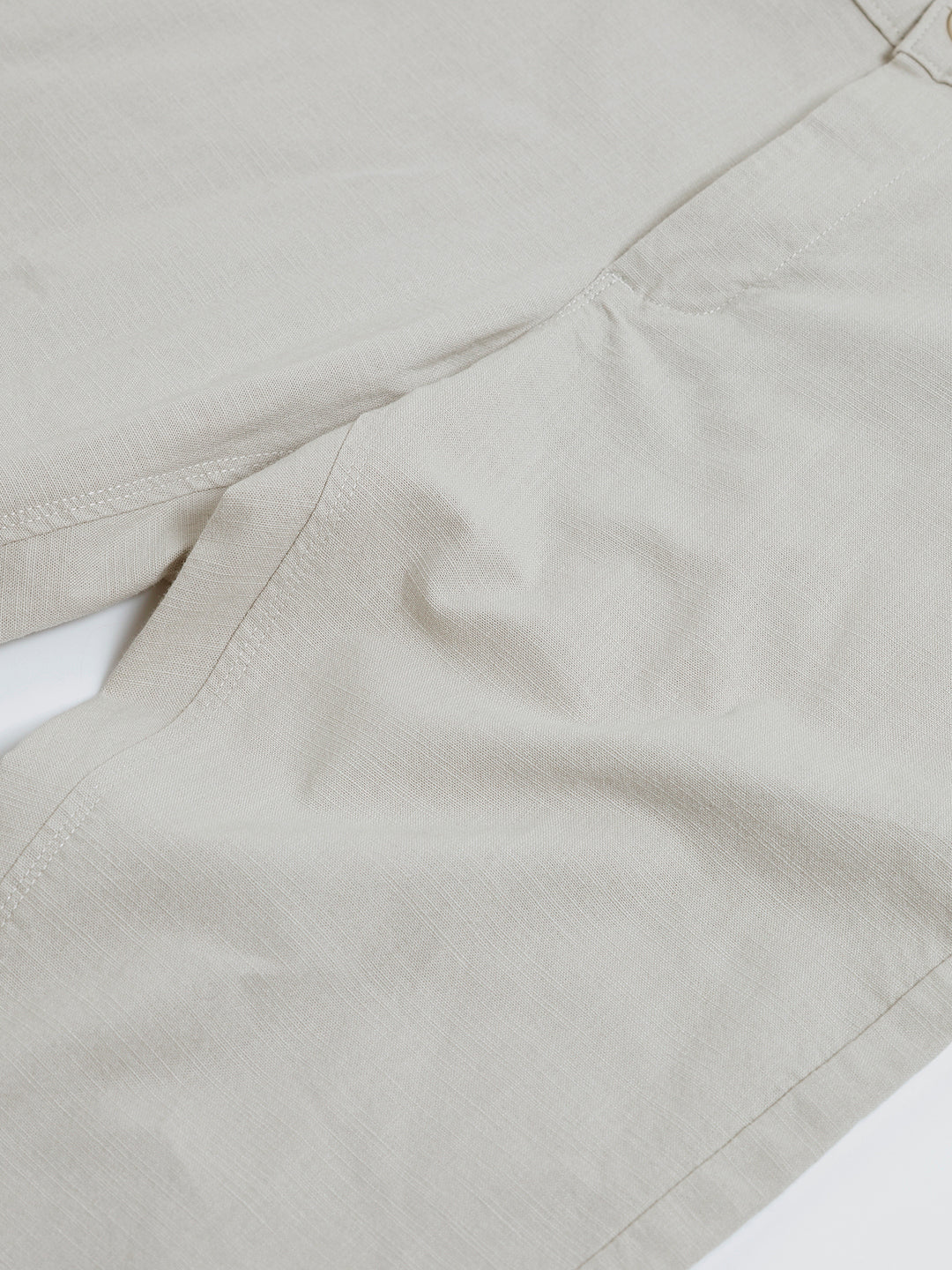 A person wearing light beige slim-fit chino pants, a navy blue t-shirt, and white sneakers, standing against a plain white studio background.