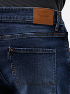 A person wearing dark blue slim-fit jeans with a faded wash, paired with a black t-shirt and white sneakers, shown from the waist down against a plain white studio background.