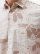 A man wearing a short-sleeve button-up shirt with a beige and brown floral pattern, paired with gray trousers, standing against a plain white background.