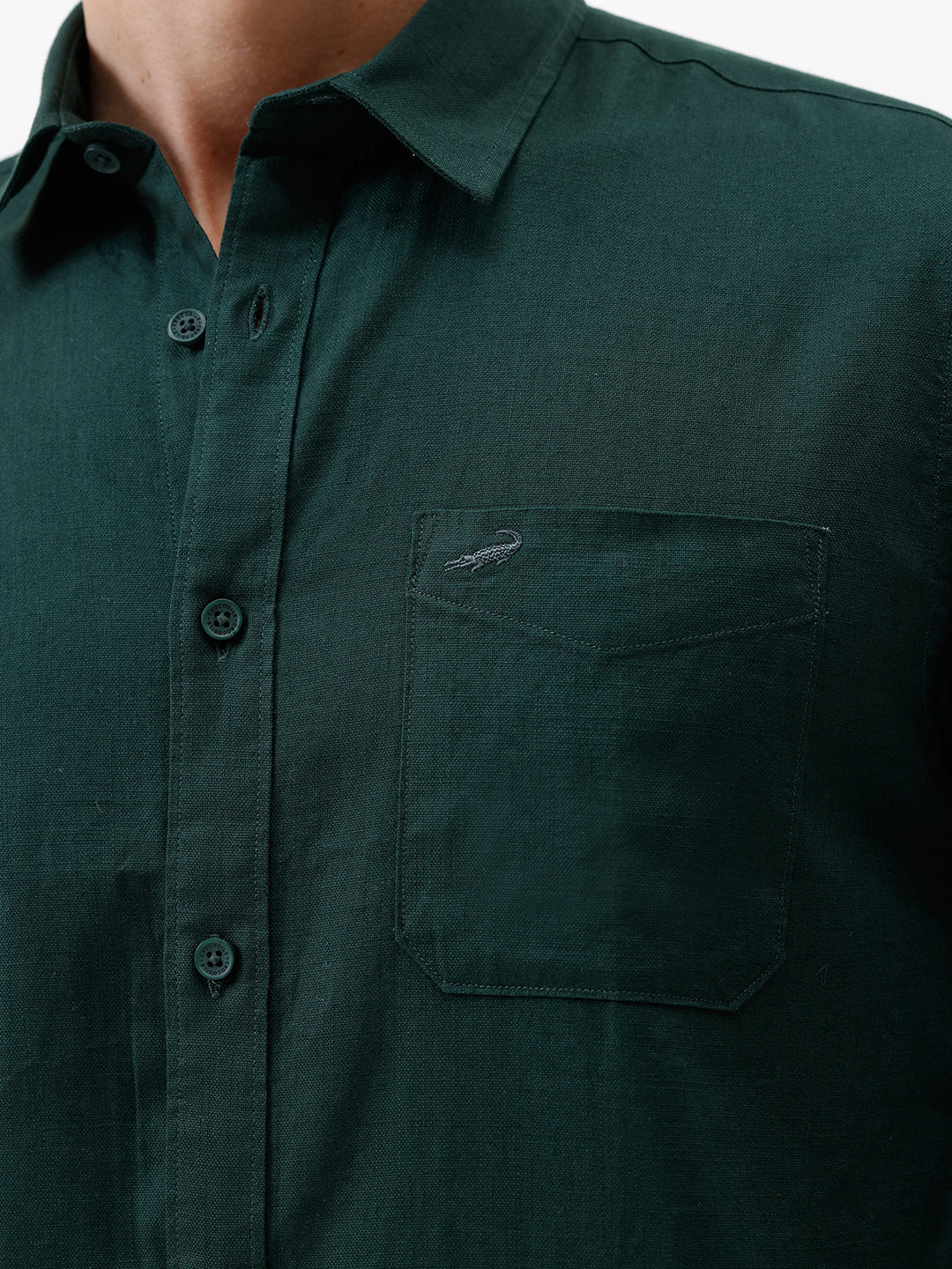 A man wearing a dark forest green long-sleeve button-down shirt with a chest pocket, paired with dark jeans, standing against a plain white studio background.