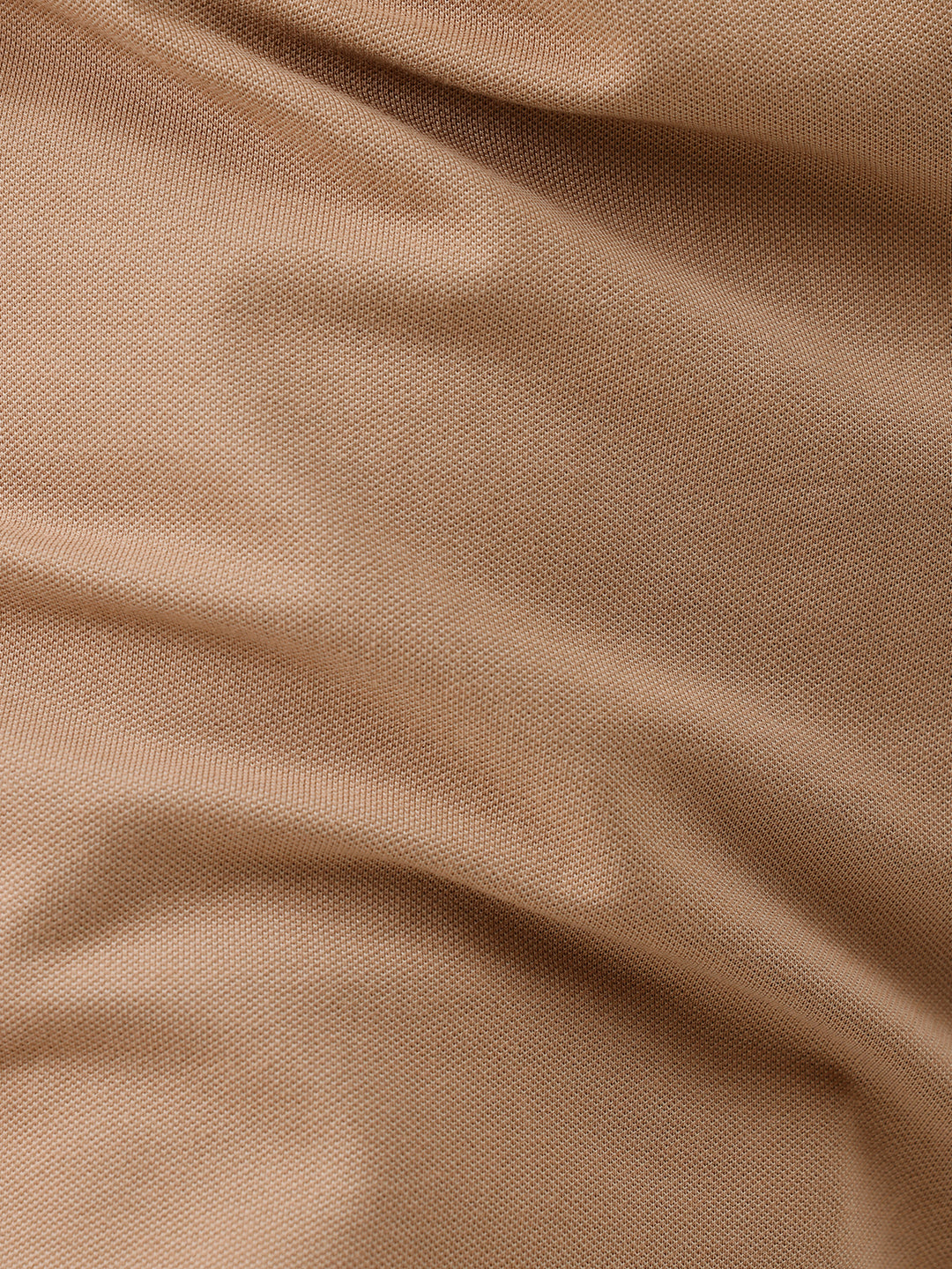 A man wearing a tan short-sleeve polo shirt with dark blue piping on the collar and sleeve cuffs, paired with dark navy pants, against a plain light gray background.