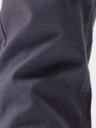 A person wearing slim-fit charcoal gray chino pants, paired with a dark purple shirt and white sneakers, standing against a plain white studio background.