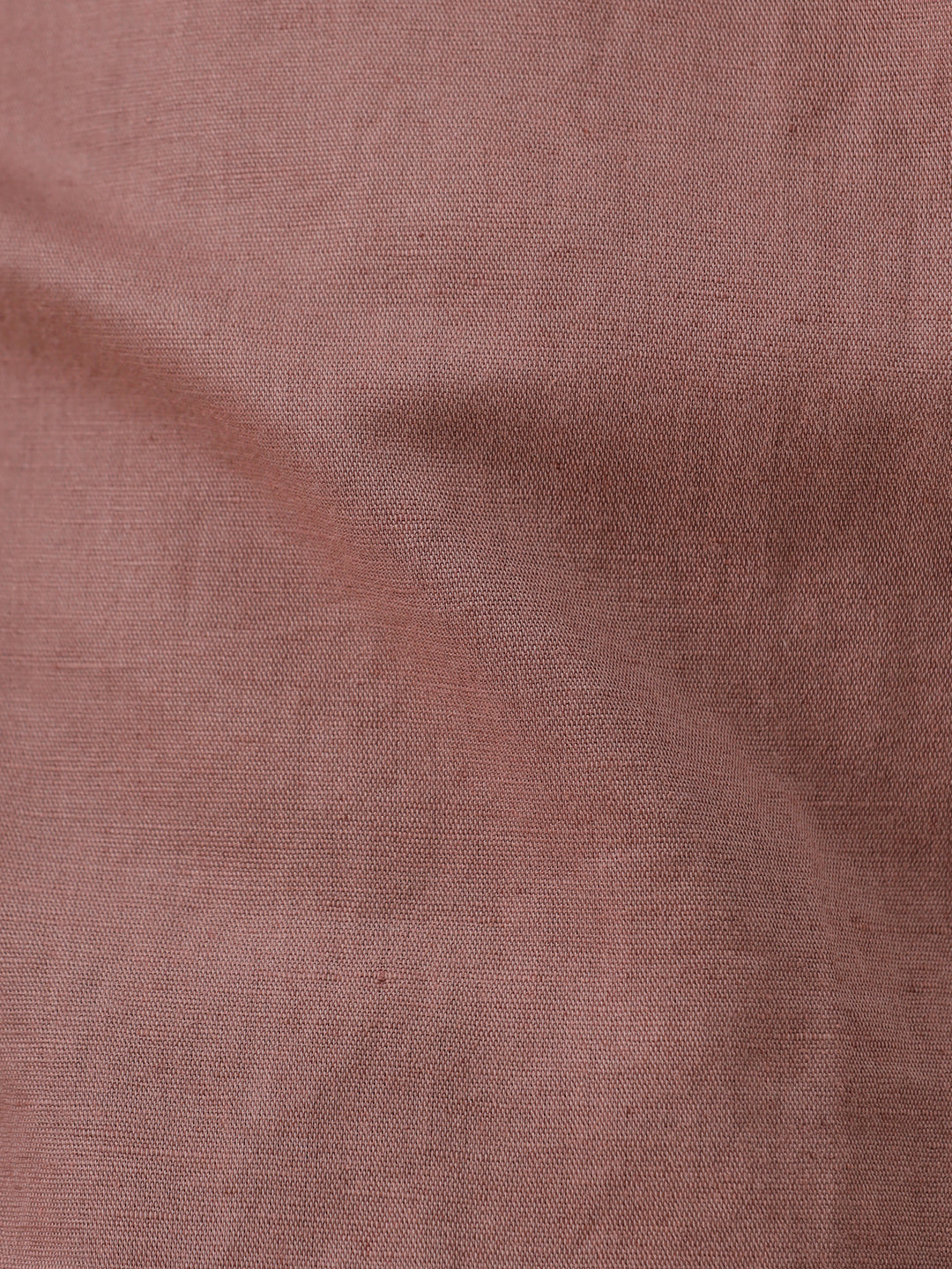 A man wearing a short-sleeve button-up shirt in a dusty rose-brown color, paired with black jeans, standing against a plain light gray background.