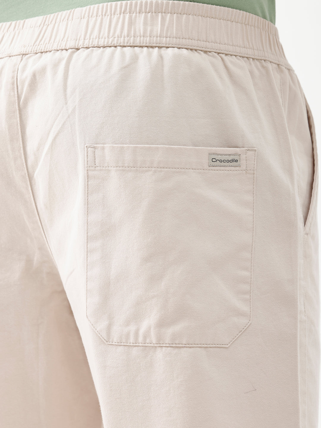 A man wearing light beige chino shorts, a sage green t-shirt, and brown suede loafers, shown from the waist down against a white studio background.