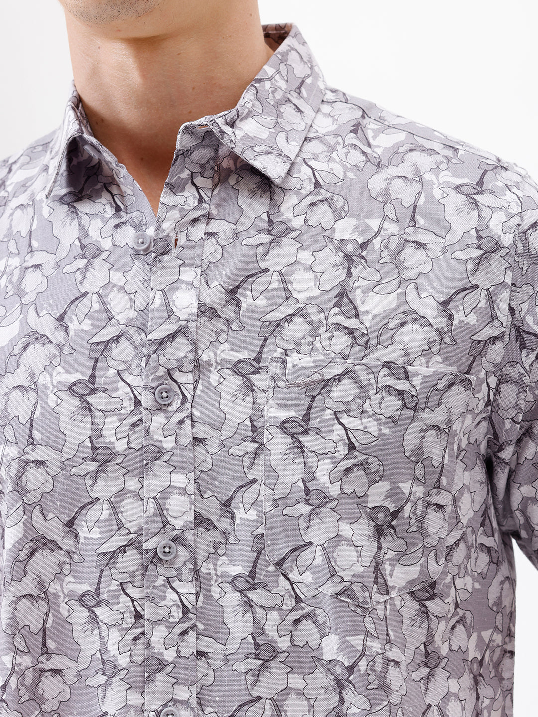 A man wearing a short-sleeve button-up shirt with a gray and white abstract pattern, paired with dark gray trousers, standing against a plain white studio background.