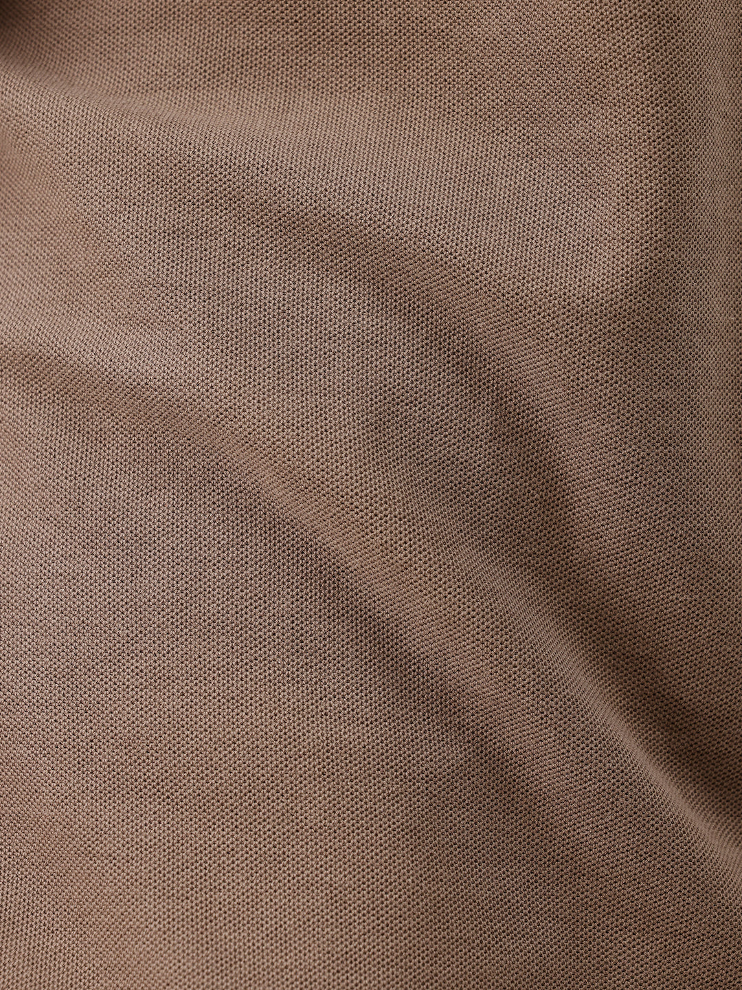 A man wearing a brown short-sleeve polo shirt with dark navy pants, standing against a plain light gray studio background.