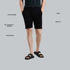 Person wearing black shorts on a gray background with text detailing fabric, fit, length, and material.