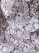 A man wearing a short-sleeve button-up shirt with a gray and white abstract pattern, paired with dark gray trousers, standing against a plain white studio background.