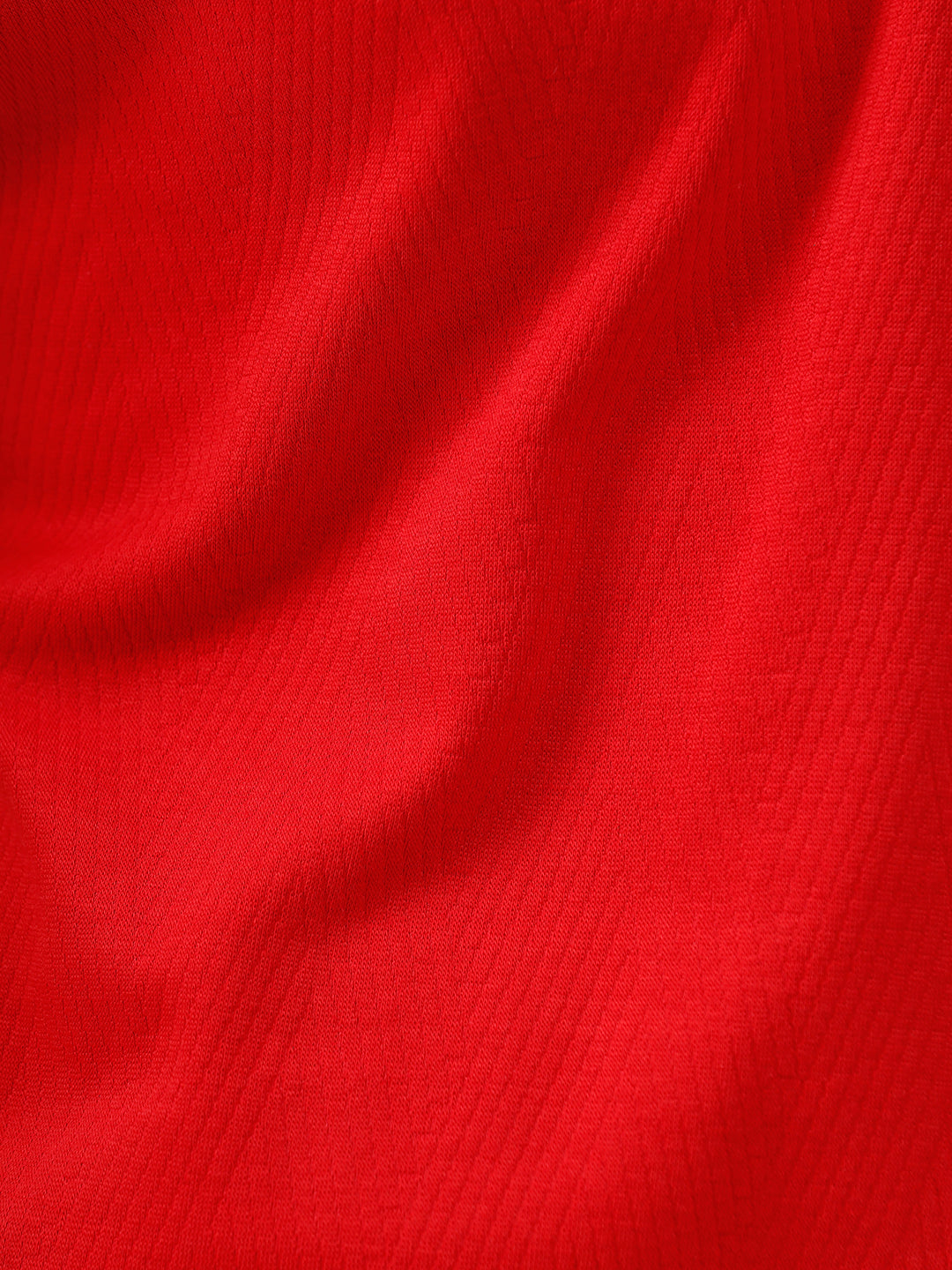 A man wearing a bright red short-sleeve polo shirt with a chest pocket, paired with beige trousers, standing against a plain white studio background.