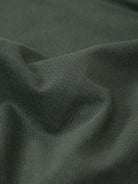 A man wearing a dark olive green short-sleeve polo shirt with a chest pocket, paired with dark jeans, standing against a plain light gray background.