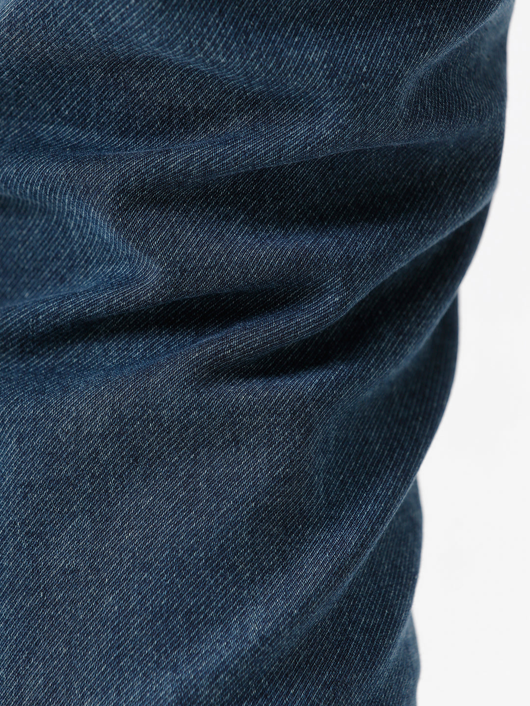 A person wearing slim-fit medium wash blue jeans, a cream-colored short-sleeve button-up shirt, and white sneakers, standing against a plain white studio background.