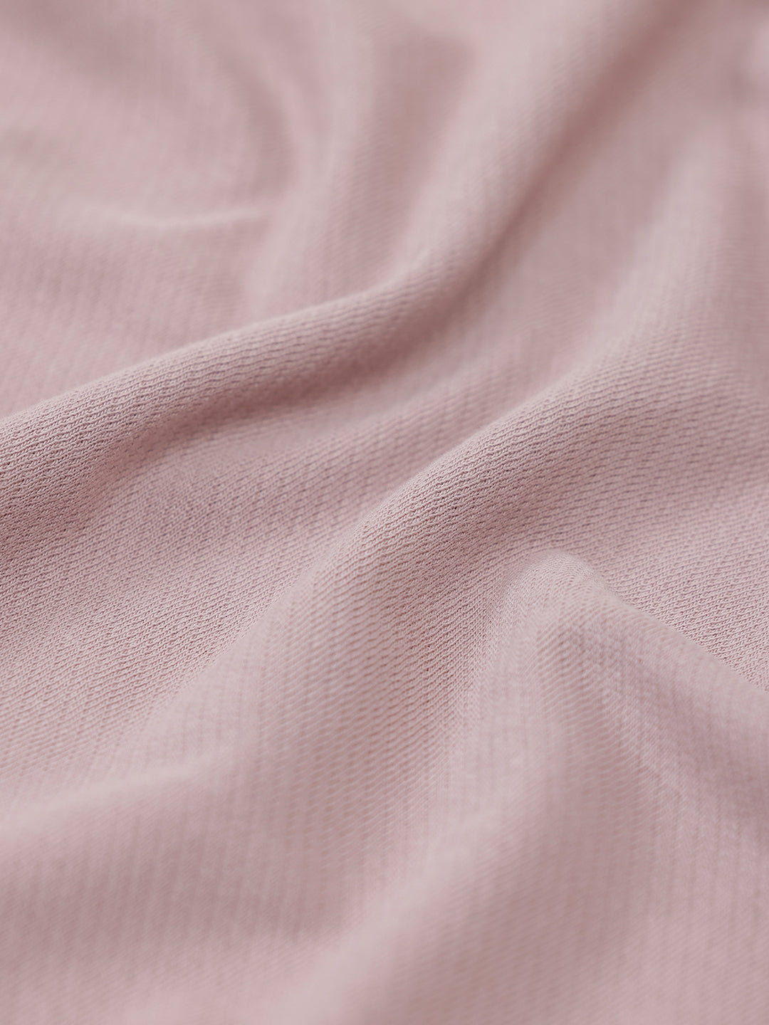 A man modeling a short-sleeve polo shirt in a dusty mauve-pink color, paired with khaki cargo pants and a baseball cap, against a plain light gray background.
