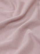 A man modeling a short-sleeve polo shirt in a dusty mauve-pink color, paired with khaki cargo pants and a baseball cap, against a plain light gray background.