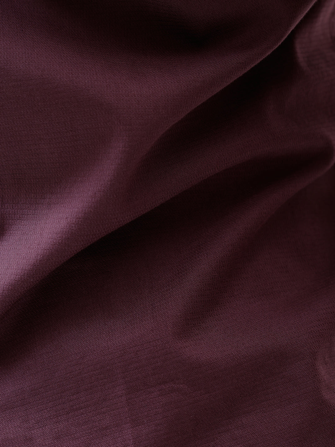 A man modeling a short-sleeve button-up shirt in a deep plum purple color, paired with gray trousers, against a plain white studio background.