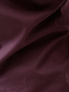A man modeling a short-sleeve button-up shirt in a deep plum purple color, paired with gray trousers, against a plain white studio background.