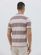 A man wearing a short-sleeve polo shirt with horizontal stripes in dusty pink and gray, paired with light beige trousers, against a plain light gray background.