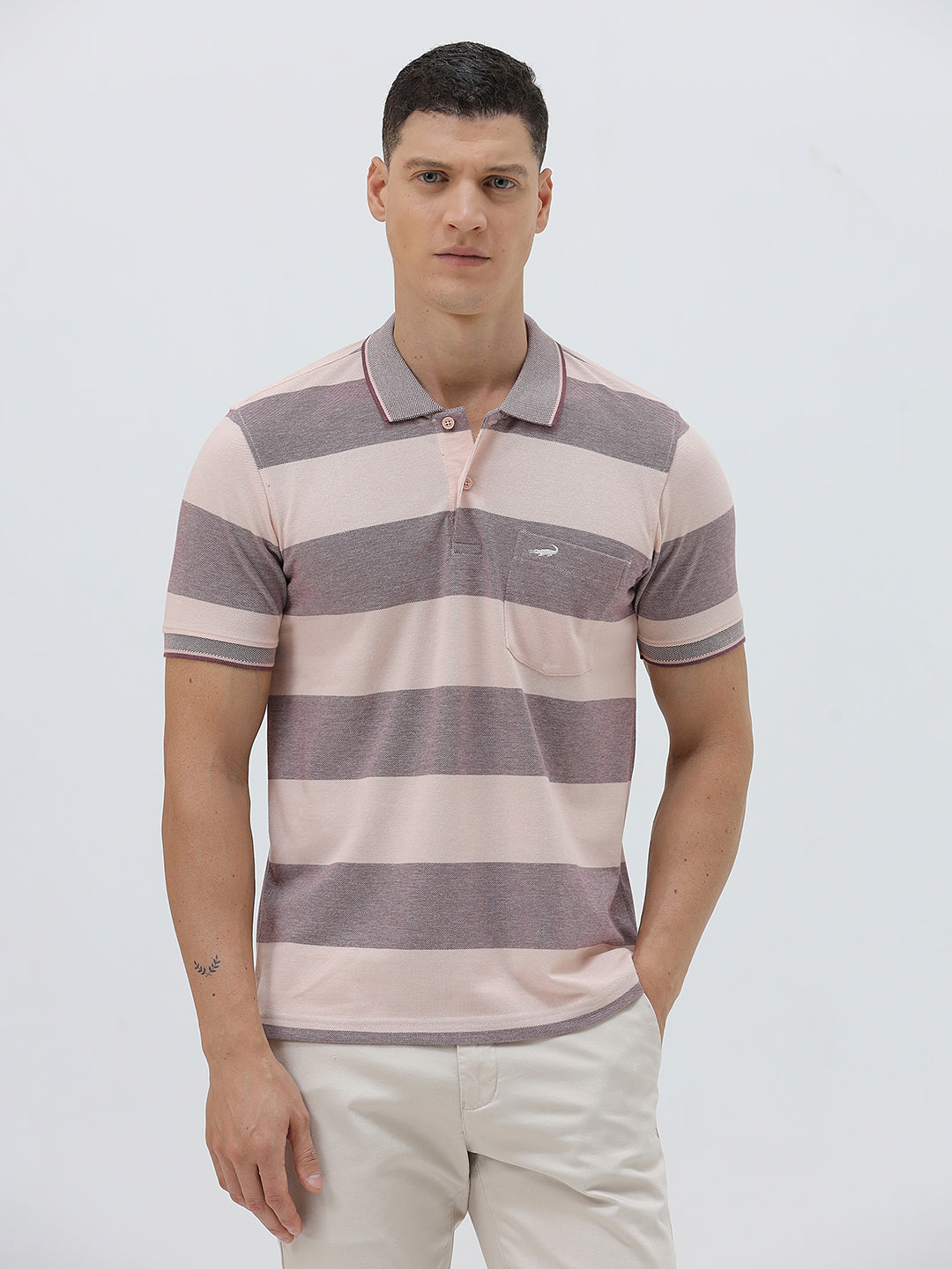 A man wearing a short-sleeve polo shirt with horizontal stripes in dusty pink and gray, paired with light beige trousers, against a plain light gray background.