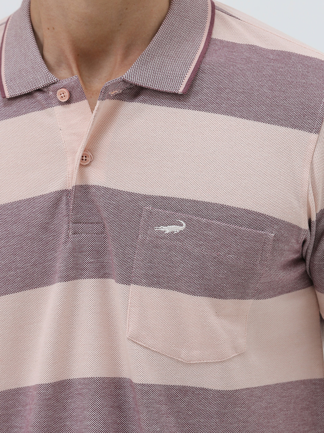 A man wearing a short-sleeve polo shirt with horizontal stripes in dusty pink and gray, paired with light beige trousers, against a plain light gray background.