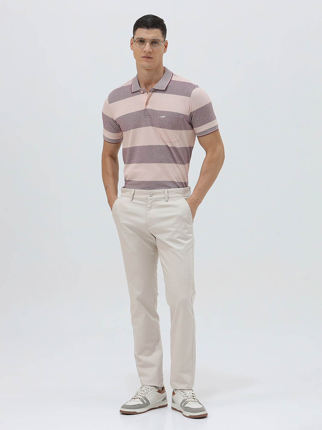 A man wearing a short-sleeve polo shirt with horizontal stripes in dusty pink and gray, paired with light beige trousers, against a plain light gray background.