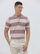 A man wearing a short-sleeve polo shirt with horizontal stripes in dusty pink and gray, paired with light beige trousers, against a plain light gray background.