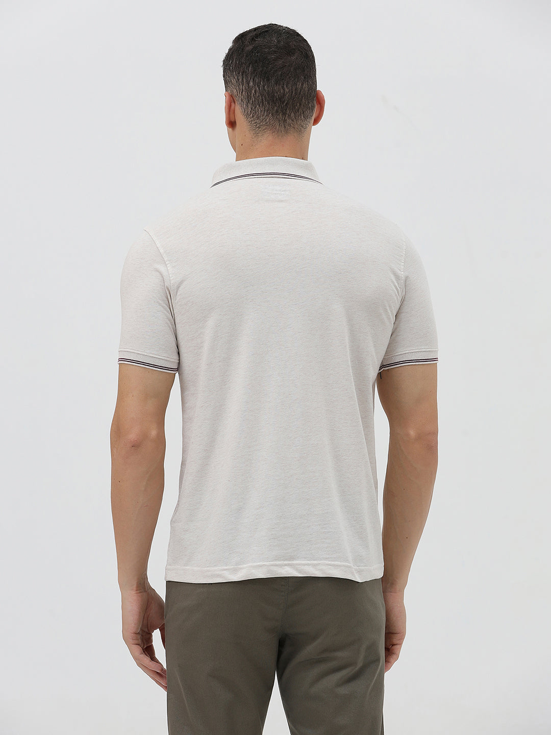 A man wearing a light beige short-sleeve polo shirt with contrasting dark gray piping on the collar and sleeve cuffs, paired with olive green trousers, against a plain light gray background.