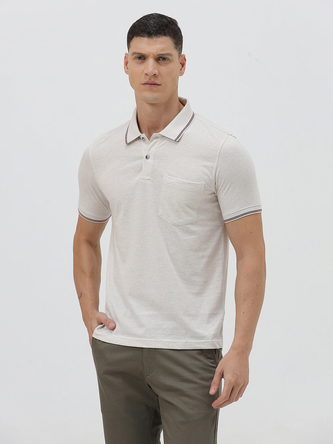 A man wearing a light beige short-sleeve polo shirt with contrasting dark gray piping on the collar and sleeve cuffs, paired with olive green trousers, against a plain light gray background.