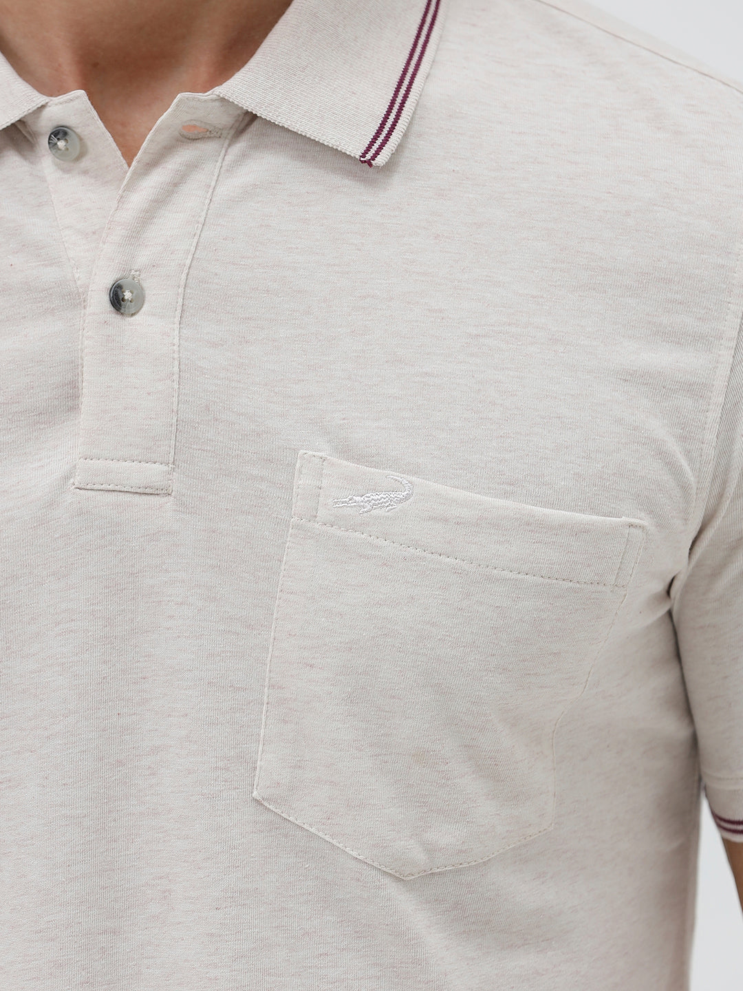 A man wearing a light beige short-sleeve polo shirt with contrasting dark gray piping on the collar and sleeve cuffs, paired with olive green trousers, against a plain light gray background.