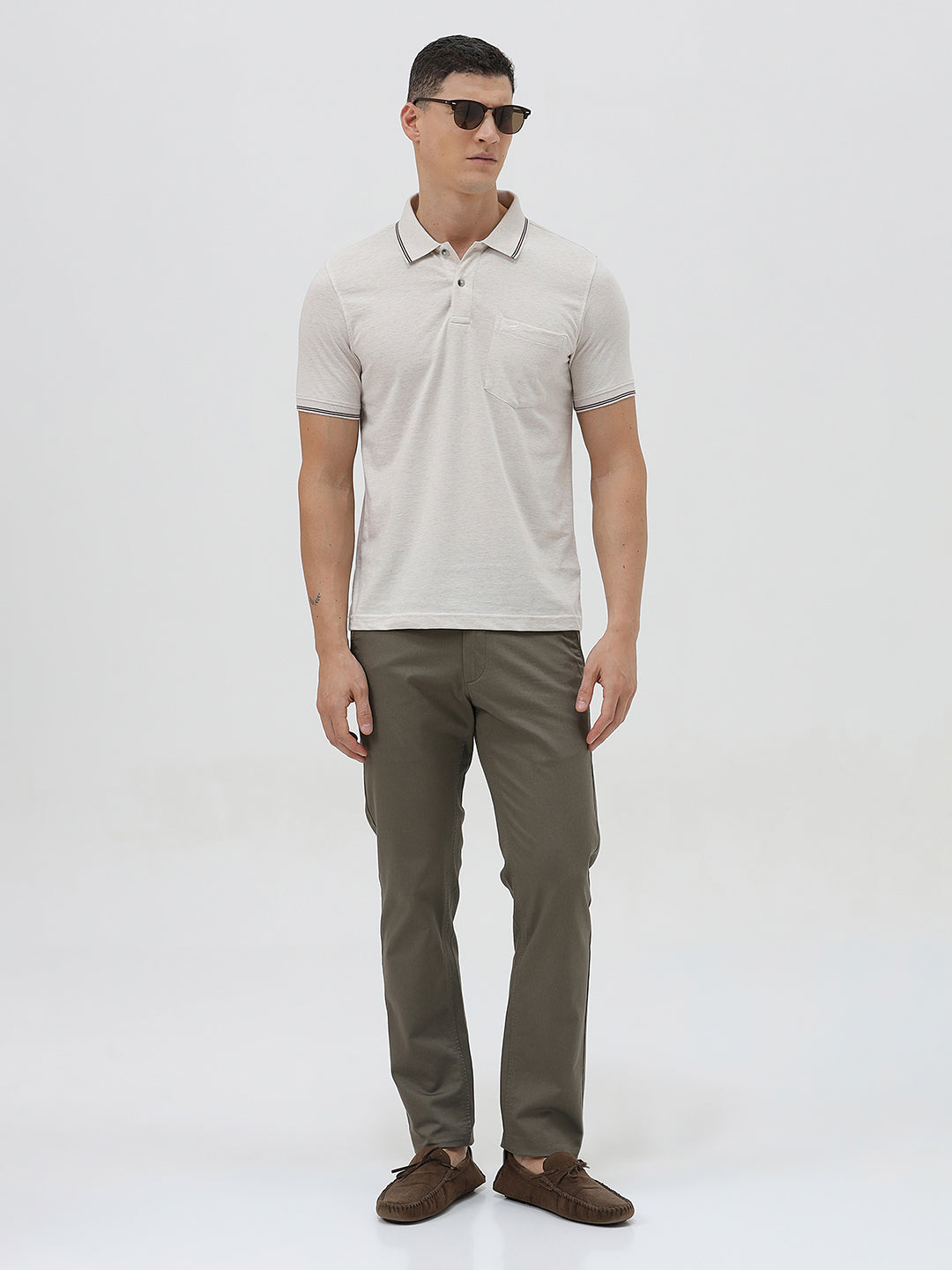 A man wearing a light beige short-sleeve polo shirt with contrasting dark gray piping on the collar and sleeve cuffs, paired with olive green trousers, against a plain light gray background.