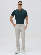 A person wearing slim-fit light beige chinos with a dark green t-shirt and white sneakers, standing against a plain white studio background.