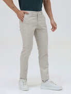 A person wearing slim-fit light beige chinos with a dark green t-shirt and white sneakers, standing against a plain white studio background.