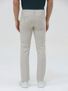 A person wearing slim-fit light beige chinos with a dark green t-shirt and white sneakers, standing against a plain white studio background.