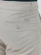 A person wearing slim-fit light beige chinos with a dark green t-shirt and white sneakers, standing against a plain white studio background.