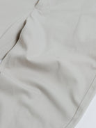A person wearing slim-fit light beige chinos with a dark green t-shirt and white sneakers, standing against a plain white studio background.