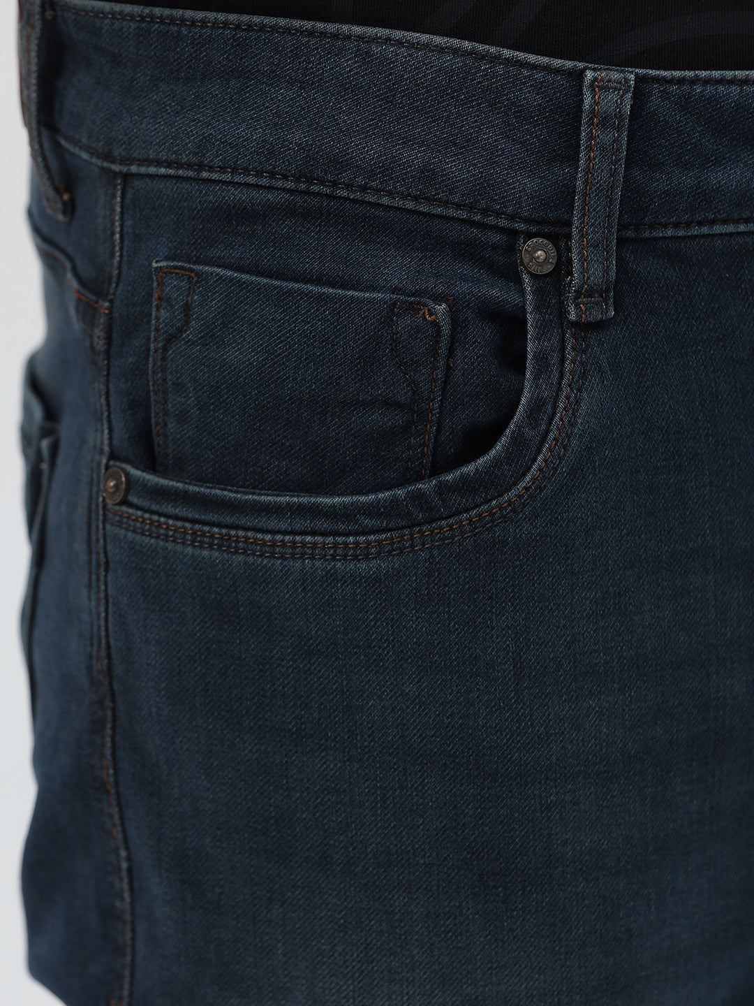 A person wearing dark blue slim-fit denim jeans, paired with a black t-shirt and navy and white sneakers, standing against a plain white studio background.