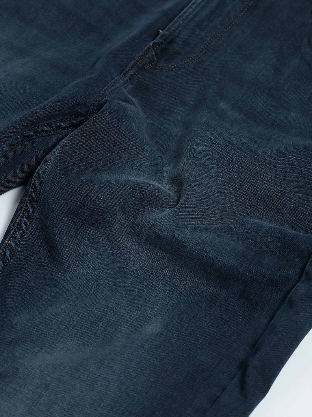 A person wearing dark blue slim-fit denim jeans, paired with a black t-shirt and navy and white sneakers, standing against a plain white studio background.