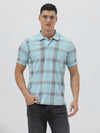 A man wearing a light blue short-sleeve polo shirt with a red and gray plaid pattern, paired with dark gray jeans, standing against a light gray studio background.